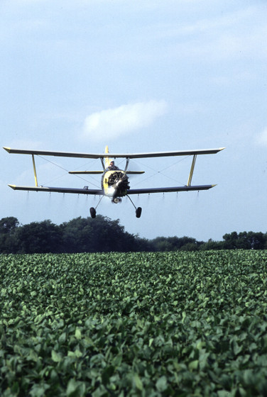 'Near Sheldon, Illinois, grower Joe Zumwalt applies a low-insecticide bait that is targeted against western corn rootworms feeding on and laying eggs in these soybeans.' Image by Ken Hammond. (from https://commons.wikimedia.org/wiki/File:Crop_Duster.jpg) This image is in the public domain because it contains materials that originally came from the Agricultural Research Service, the research agency of the United States Department of Agriculture.